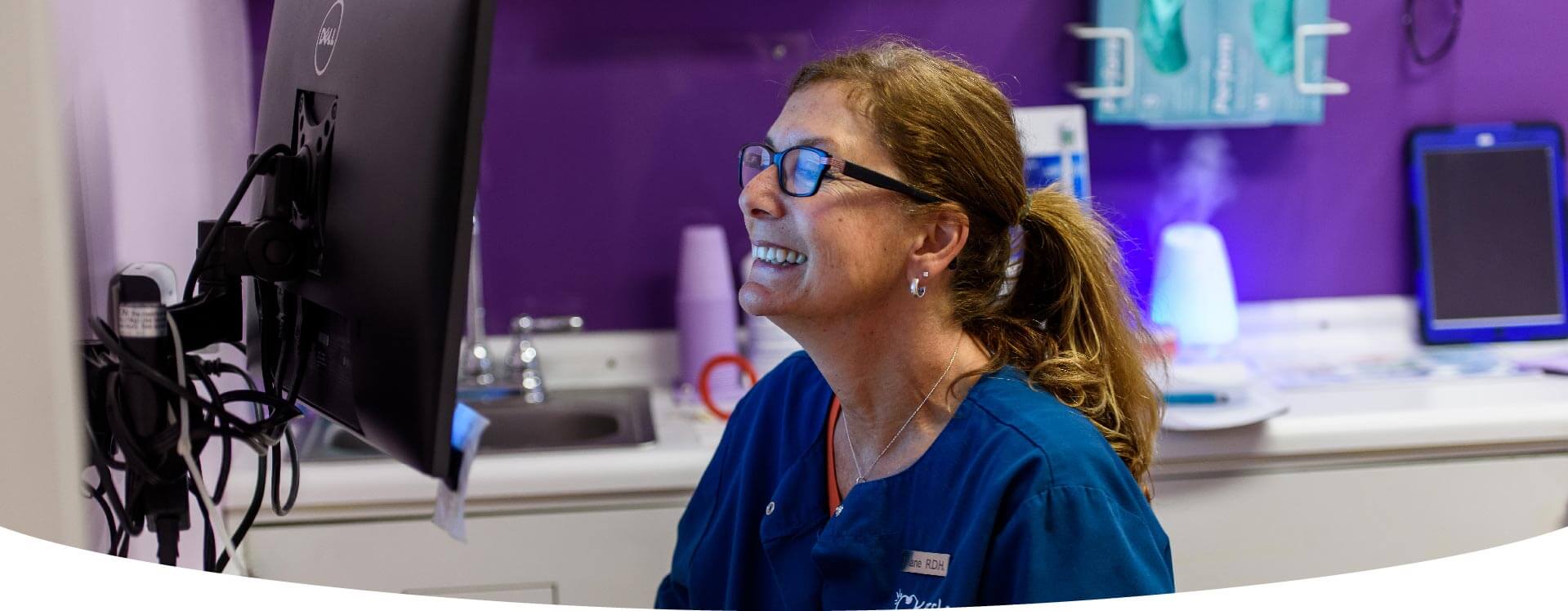 A Lady In a Dental Office Looking At A Computer And Smiling